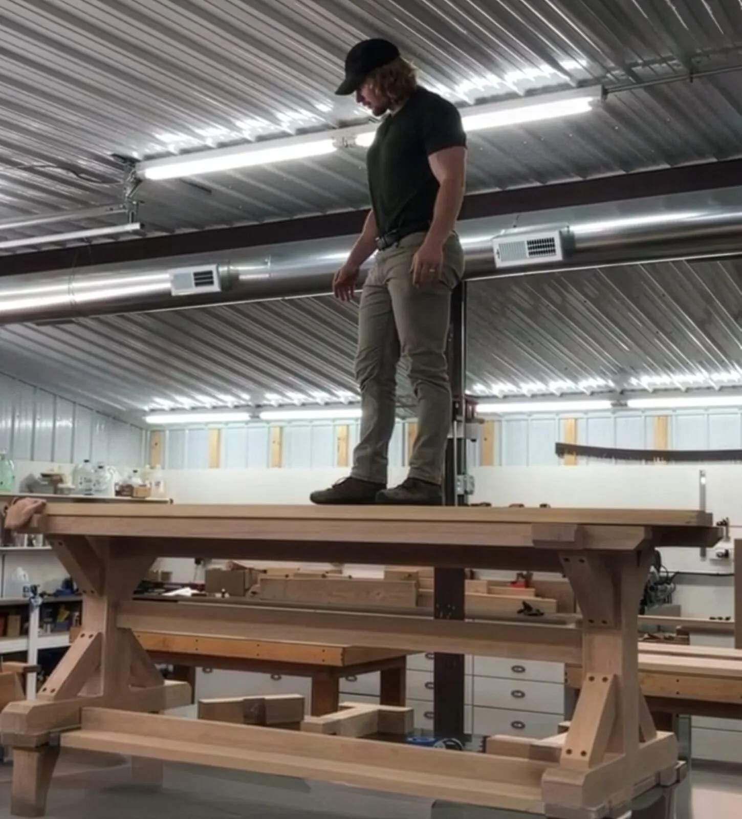Kevin Root standing atop a large white oak table he built in the studio